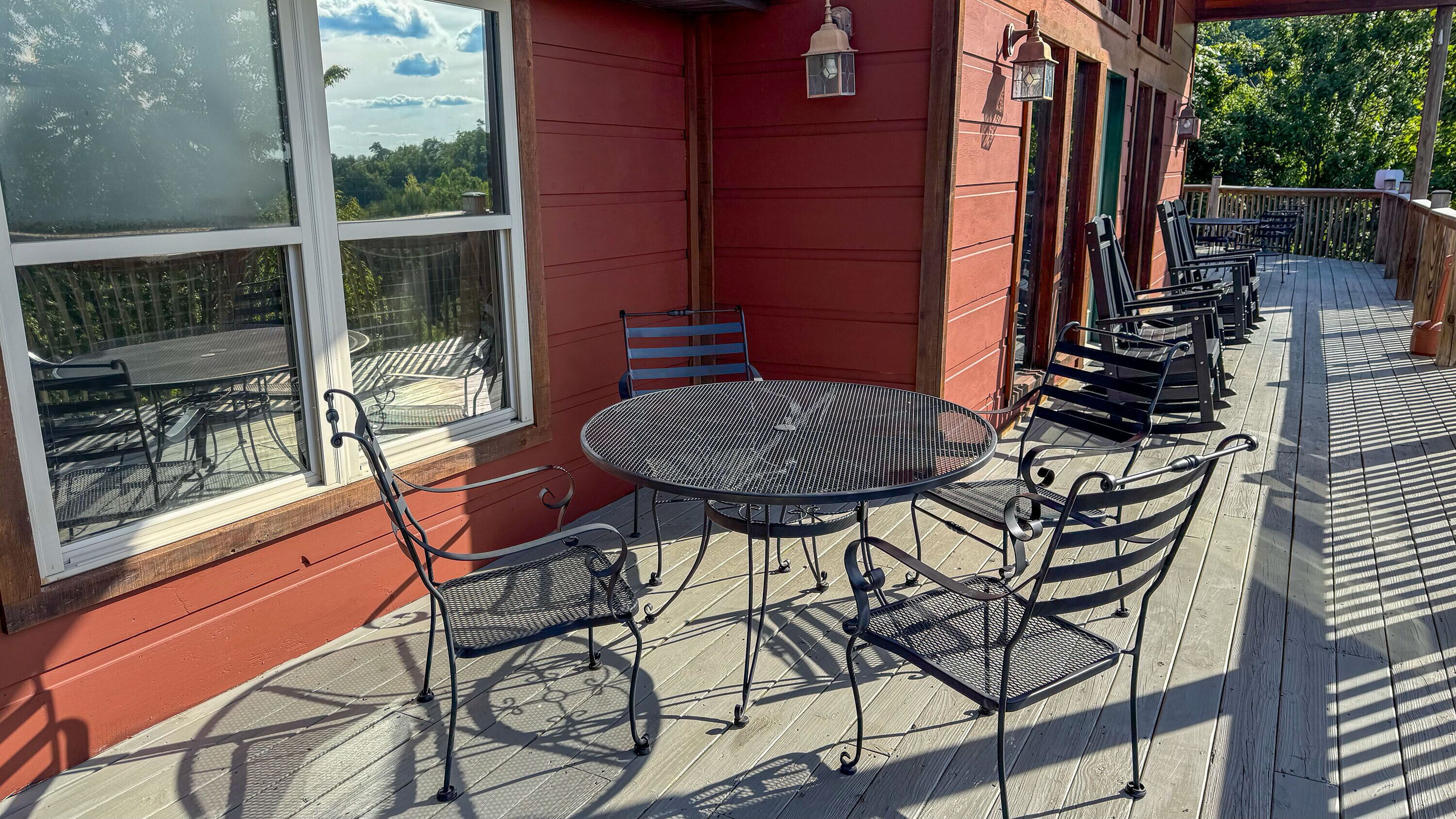 Eine überdachte Terrasse mit einem runden Metalltisch und Stühlen, großen Fenstern und einem Holzboden.