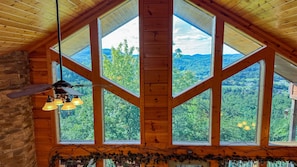 A room with large windows, a ceiling fan, and a rustic decor.