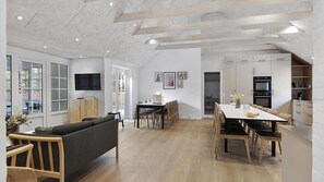 Un interior moderno con comedor, cocina y sala de estar, destacando un techo alto y ventanas amplias.