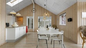 Eine geräumige Küche mit einem langen Esstisch, Holzwänden und einer hohen Decke mit Oberlichtern.
