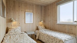 A room with two single beds, a small bedside table, a framed picture on the wall, and a window with a view.
