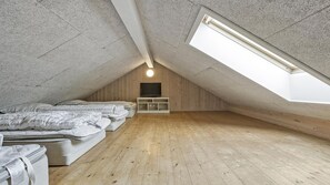 Ein kleines Schlafzimmer im Dachgeschoss mit geneigter Decke, Holzboden, einem Bett, einem Fernseher und einem Oberlicht.