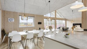 Un vaste espace de salle à manger avec une longue table et des chaises, un îlot de cuisine avec des sièges, et de grandes fenêtres qui laissent entrer la lumière naturelle.