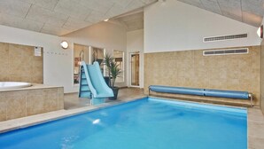 Une piscine intérieure avec un toboggan bleu, un jacuzzi et un espace de détente avec un banc bleu.