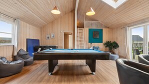 A pool table in a room with wooden walls and a skylight. There are bean bags and a foosball table.