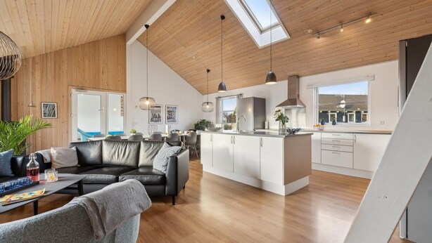A spacious living area with a black leather sofa, a dining table, and a kitchen with white cabinets and a large island.
