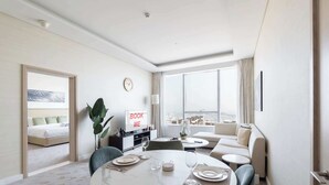 Ein modernes Hotelzimmer mit Essbereich, einer Couch, einem Fernseher und einem großen Fenster mit Blick auf die Stadt.