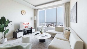 Ein modernes Hotelzimmer mit einem großen Fenster, einer Couch, einem Couchtisch, einem Fernseher und einem Schild mit der Aufschrift 'BOOK ME'.