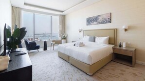 Habitación de hotel con una cama grande, un escritorio, una silla, una mesita y un ventanal con vistas a la ciudad.