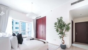Ein modernes Schlafzimmer mit Bett, Nachttisch, großem Fenster, einem roten Kleiderschrank und einer Zimmerpflanze.