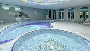 Ein moderner, überdachter Schwimmbereich mit einem einzigartigen geometrischen Design und großzügiger Gestaltung, durchflutet von natürlichem Licht.