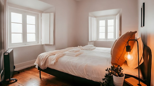 Ein Schlafzimmer mit einem Bett, einer Nachttischlampe, einer Heizung und Fenstern.
