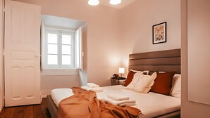Ein Schlafzimmer mit einem Bett, einem Nachttisch, einer Lampe, einem Fenster und einer Tür.
