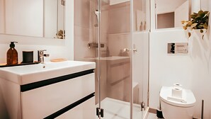 Ein modernes Badezimmer mit Duschkabine aus Glas, einem weißen Waschbecken mit schwarzer Linie und einer Toilette.