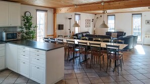A spacious kitchen with a central island, dining area with chairs, a sofa, and a large window providing natural light. - VillaVilla 78 - Öland, Sverige (Köpingsvik)