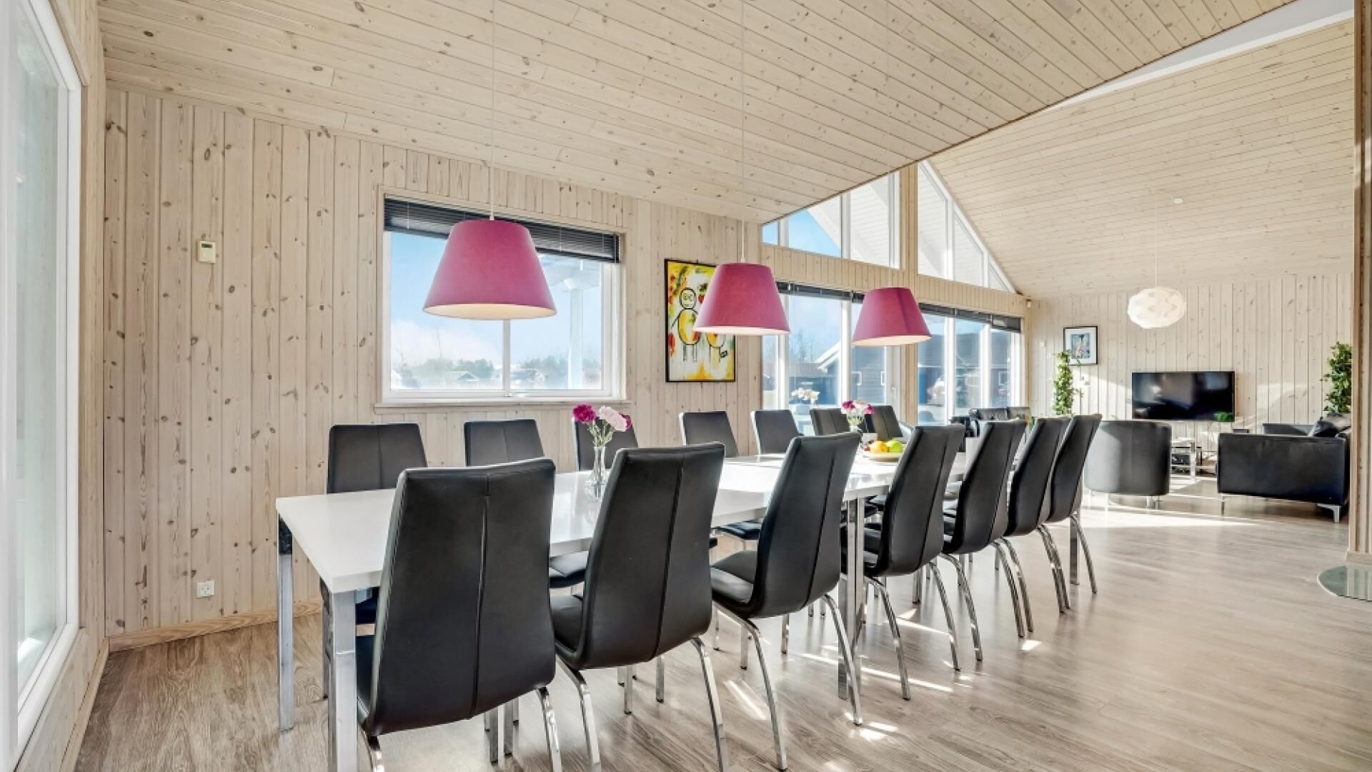 Un'ampia sala da pranzo con un lungo tavolo e sedie nere, grandi finestre e un soffitto alto con travi in legno.
