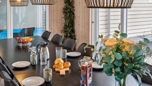 A dining table set with plates, glasses, a pitcher, a bowl of fruit, croissants, and a carton of milk.