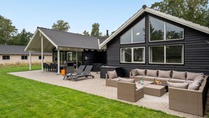 A modern house with a covered patio, outdoor furniture, and a grill.