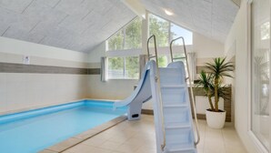 An indoor swimming pool with a blue slide, large windows, and a potted plant.