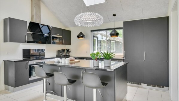 Una cocina moderna con una isla central, taburetes de bar y un amplio ventanal que proporciona luz natural.