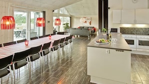 Een moderne keuken met een centraal eiland, een eethoek met een lange tafel, en hanglampen.