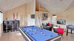 Een pooltafel met ballen, een bar, een bank en een tafelvoetbal in een ruimte met houten wanden en een hoge plafond.