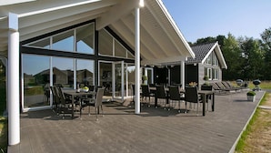 Une maison moderne dotée d’un patio couvert, aménagé avec du mobilier d’extérieur et un barbecue.