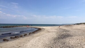 Een zandstrand met een rotsachtige kustlijn, helderblauwe lucht en een rustige zee.