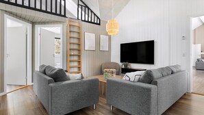 Een moderne woonkamer met een grijze zithoek, een houten ladder, een televisie en een houten vloer.
