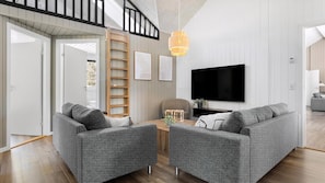 A modern living room with a grey sofa set, a wooden ladder, a TV, and a wooden floor.