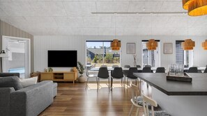 Un salon moderne doté d’un téléviseur à écran plat, d’un canapé gris, d’un coin repas avec des chaises et une table, ainsi que d’un îlot de cuisine avec un bar.