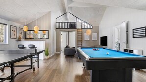 Een moderne woonkamer met een biljarttafel, een bank en een eethoek met een tafel en stoelen.