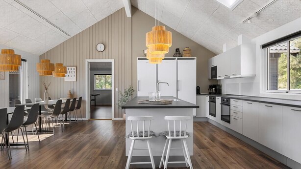 Een moderne keuken met een centraal eiland, hanglampen en een eethoek met stoelen en een tafel.