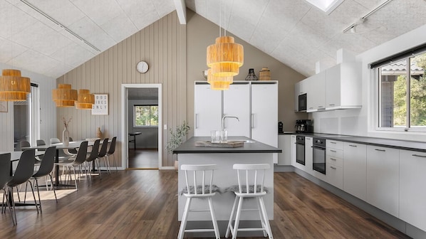 A modern kitchen with a central island, pendant lights, and a dining area with chairs and a table.
