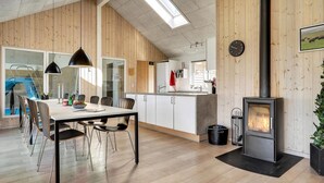Une cuisine moderne avec des murs en bois, un coin repas avec une table et des chaises, une horloge bien visible et un poêle à bois.