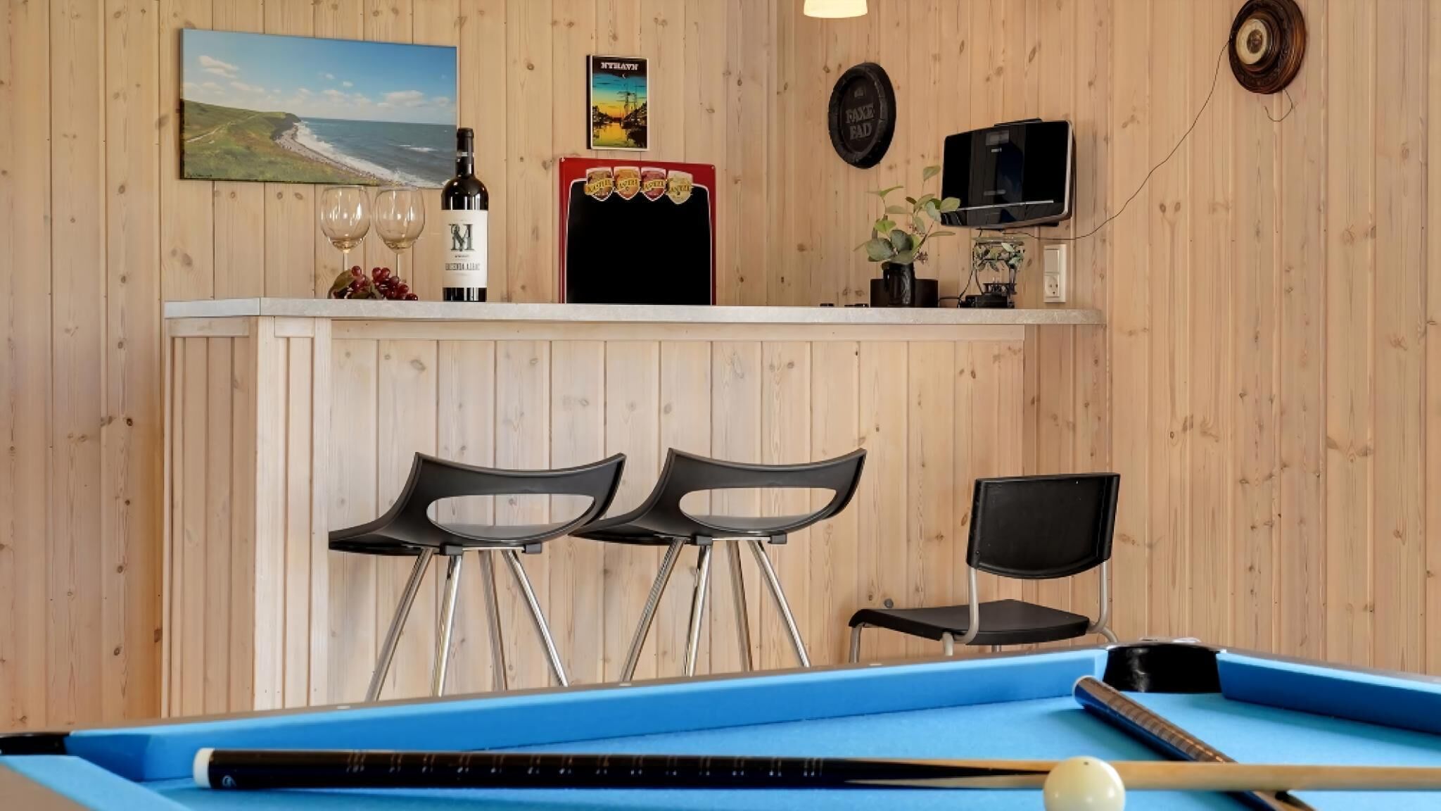 Uma área de bar com dois bancos, mesa de bilhar, garrafa de vinho e televisão.