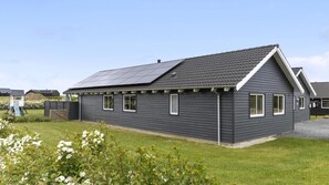 Ein eingeschossiges Haus mit dunkelgrauem Anstrich, weißem Zierwerk und einem geneigten Dach mit Solaranlage.