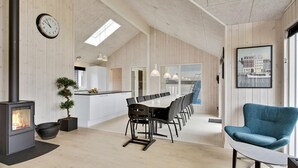 A modern kitchen with a dining area, a large wooden-framed window, and a clock on the wall.