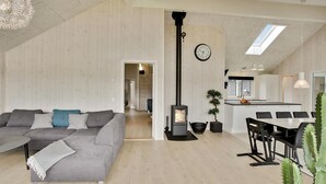 A modern loft-style living space with a gray sofa, a dining area, a kitchen, and a wood-burning stove.