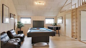 A room with a pool table, a leather sofa, and a television.