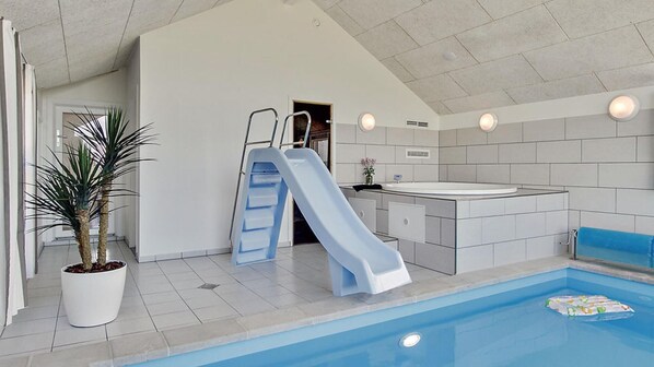 An indoor pool with a slide, a small sink, and a potted plant.