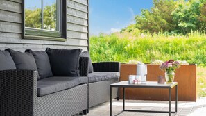 A modern outdoor seating area with a gray sofa, a small table, and a vase of flowers.