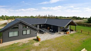 Ein modernes Haus mit einer großen Terrasse, einem überdachten Sitzbereich im Freien und einem großzügigen Innenraum mit Essbereich.