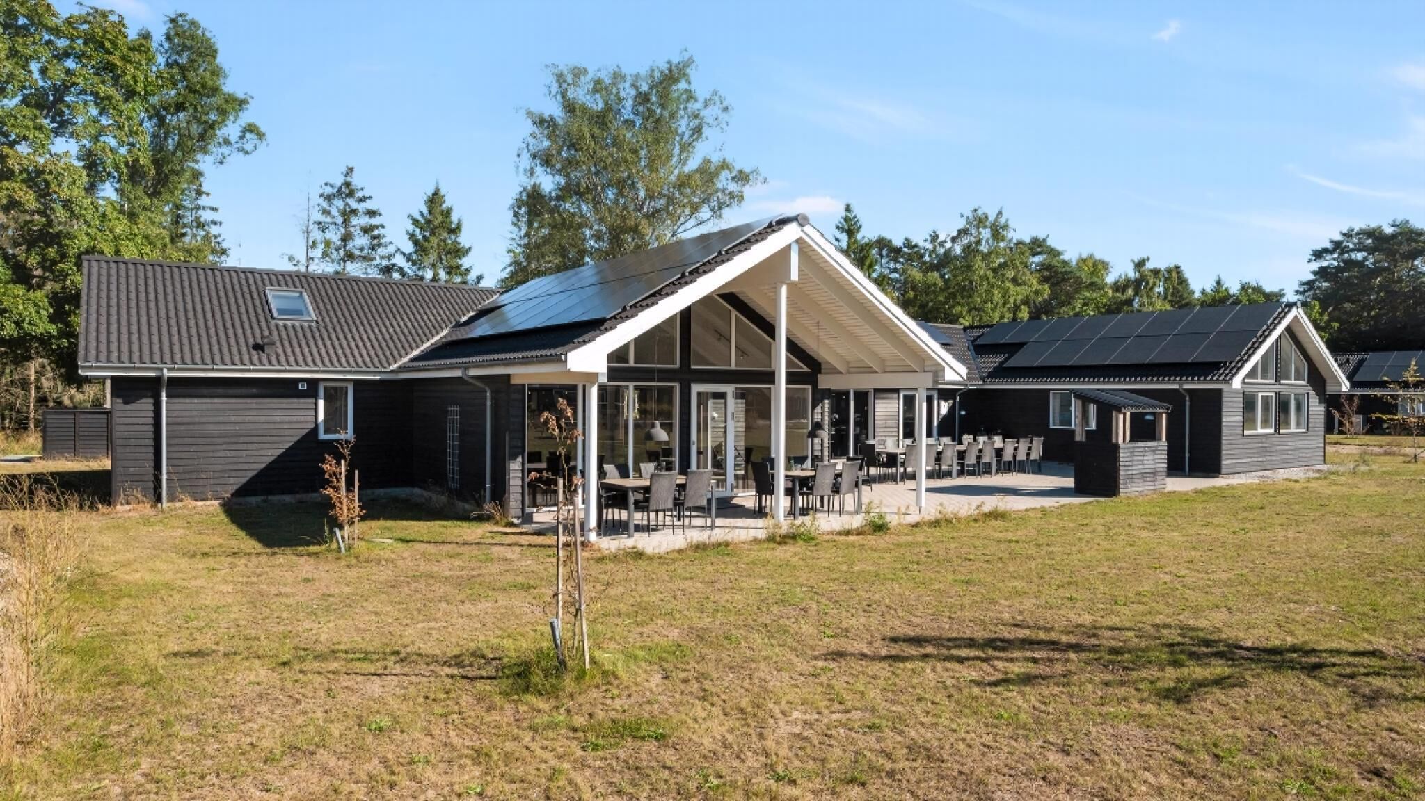 A modern house with a covered patio, a separate dining area, and a solar panel roof.