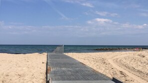 Une plage avec une promenade pavée menant à l’eau, une côte rocheuse et un ciel dégagé.
