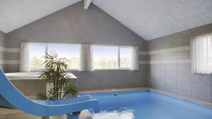 En inomhuspool med en blå vattenrutschkana, två fönster med gardiner och en växt.