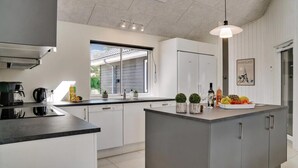 A modern kitchen with a central island, built-in appliances, and a large window. - VillaVilla 503 - Marielyst, Lolland/Falster/møn (Væggerløse)