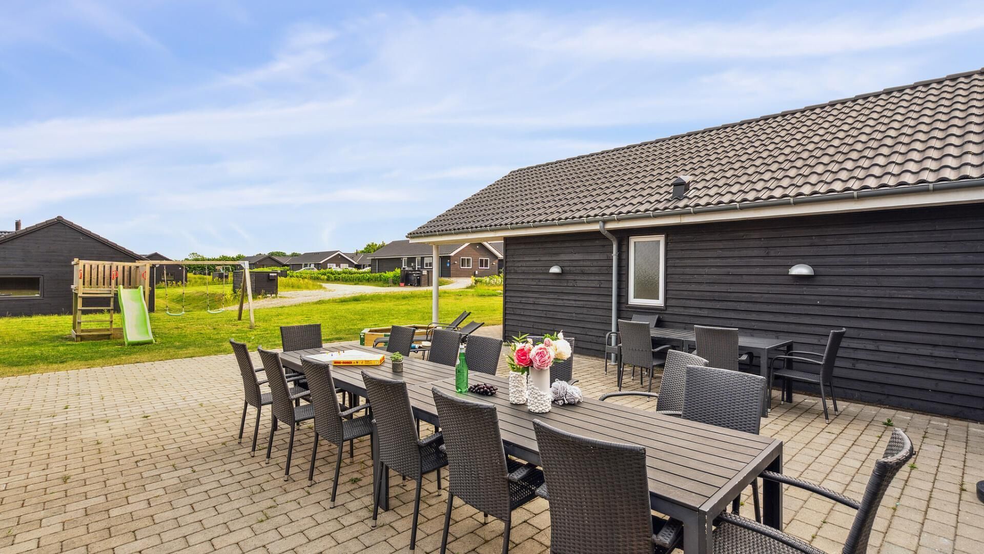 An outdoor patio area with a table and chairs, a children's playset, and a view of neighboring houses.