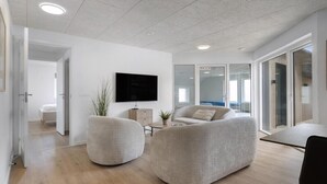 Een moderne woonkamer met een flatscreen televisie, twee ronde zithoeken, een houten vloer en een glazen deur naar een balkon.