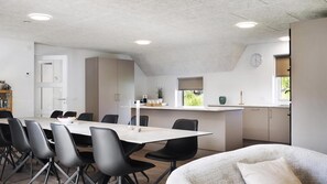 Cozinha moderna com área de jantar, destacando uma mesa comprida, cadeiras pretas e bancada com pia e armários.